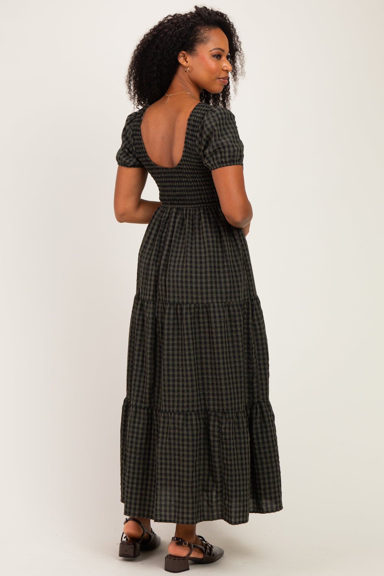 woman wearing a black and green checked maxi dress with puff sleeves and a smocked bodice, shown from the back