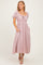 woman wearing a light pink midi dress with puff sleeves, a tie front neckline, and pockets, styled with strappy sandals
