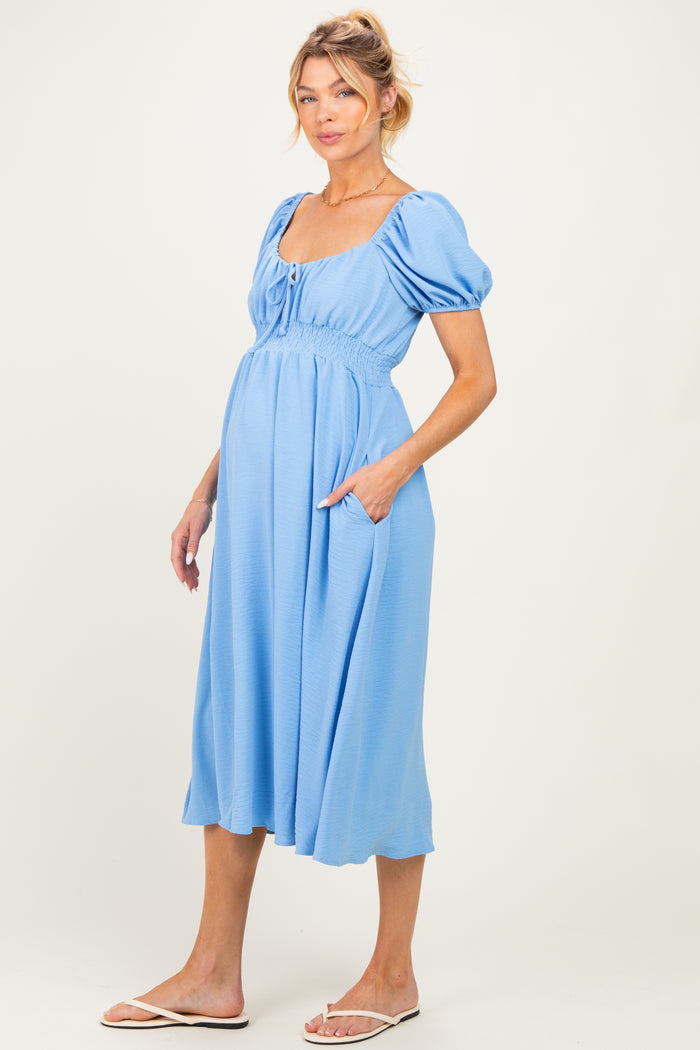 woman wearing a light blue maternity dress with puff sleeves and side pockets, showcasing her baby bump