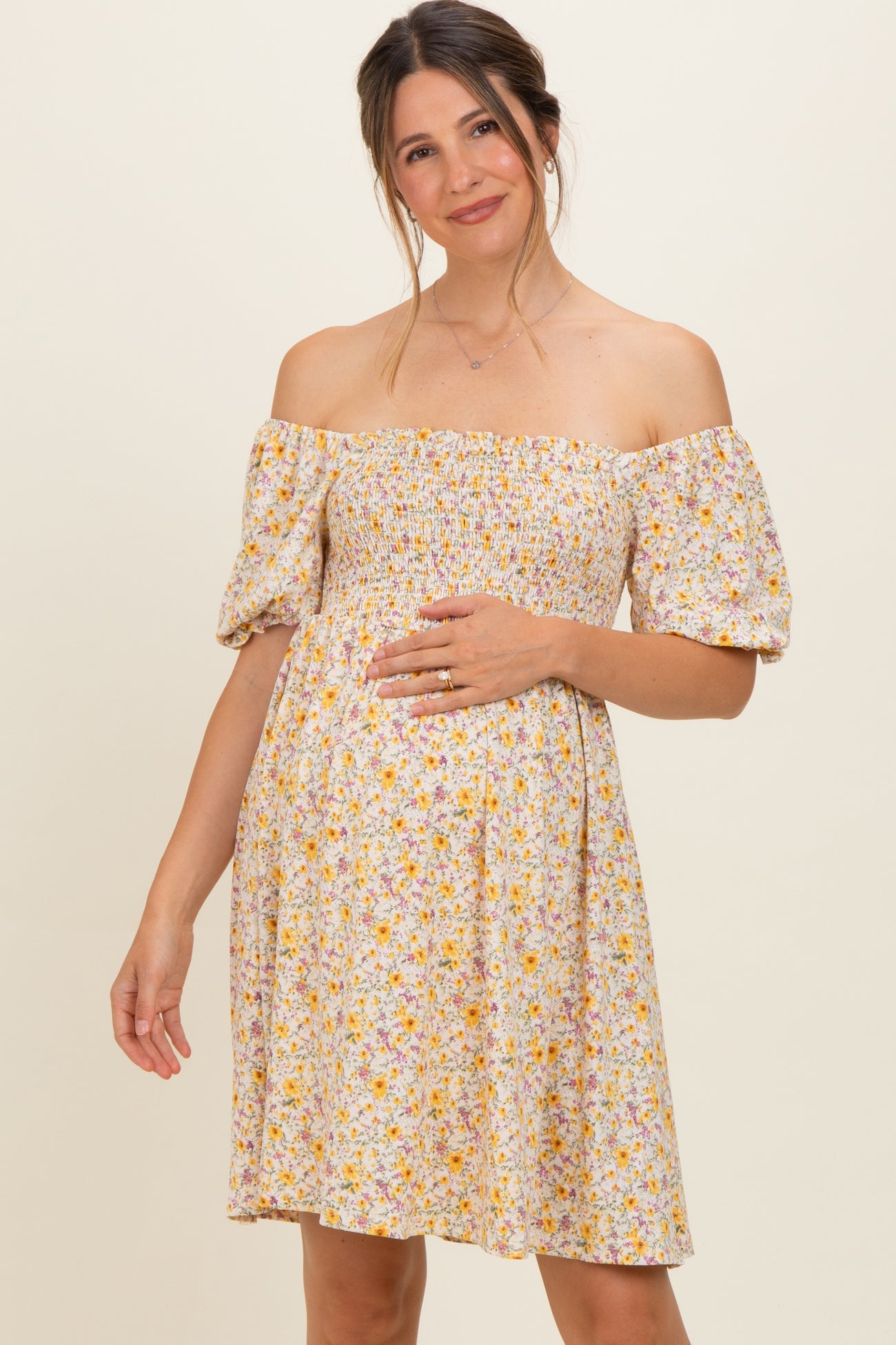 woman wearing a floral off-the-shoulder maternity dress with a smocked bodice and holding her baby bump