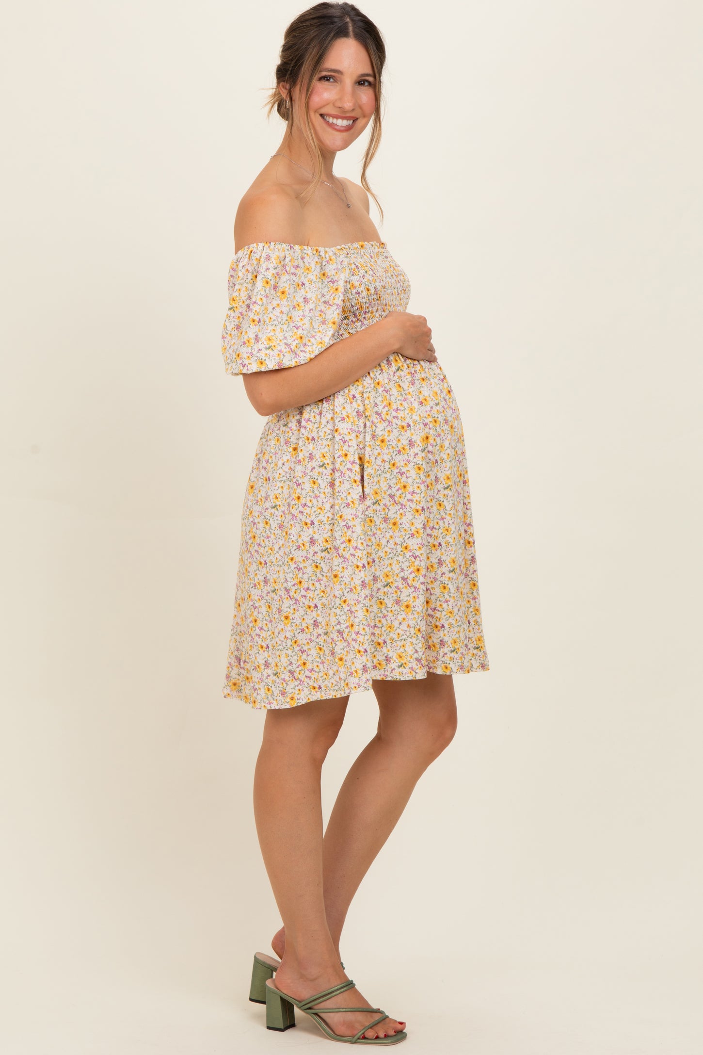 woman wearing a yellow floral off-the-shoulder maternity dress and holding her baby bump
