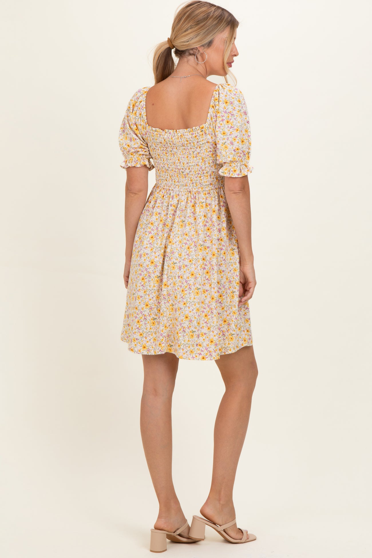 woman wearing a yellow floral smocked dress with puff sleeves, showing the back view