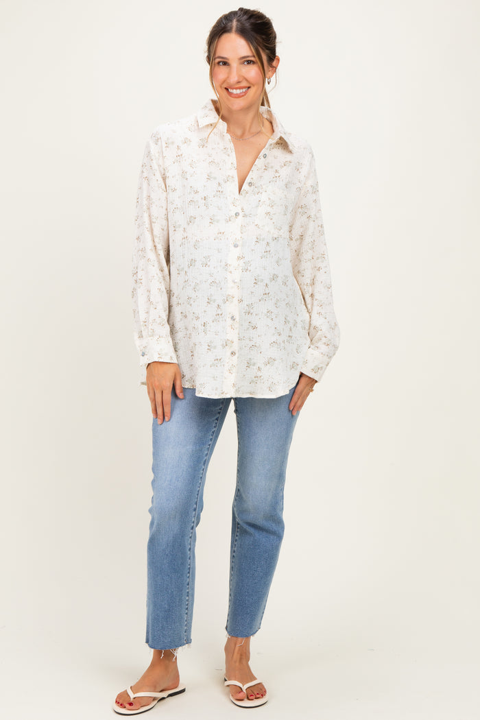 woman wearing a floral print maternity shirt and light blue jeans, standing and smiling with a relaxed posture