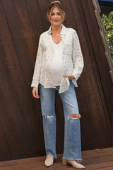 woman wearing a white floral maternity shirt over a white tank top and distressed blue maternity jeans, showing her baby bump