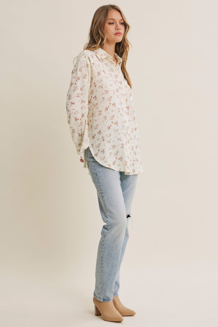 woman wearing a cream floral button-up shirt and light blue distressed jeans with beige heels