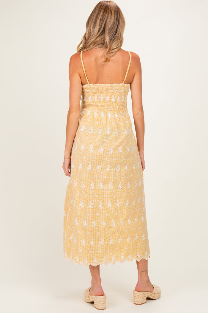 woman wearing a yellow maternity maxi dress with floral embroidery and adjustable straps, showing the back view