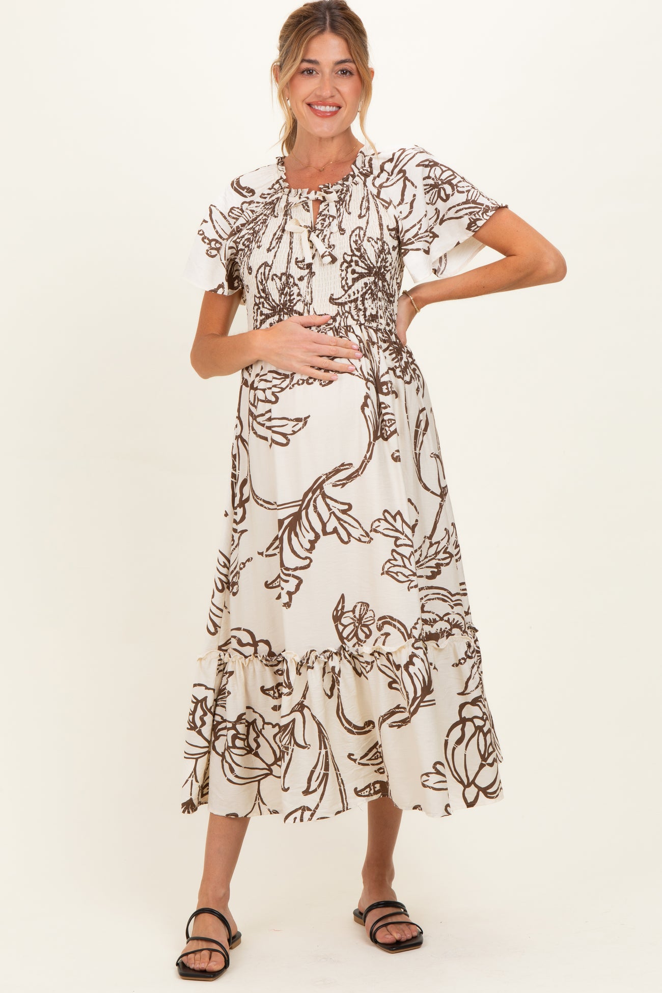 woman wearing a maternity floral print maxi dress with ruffle hem and holding her baby bump