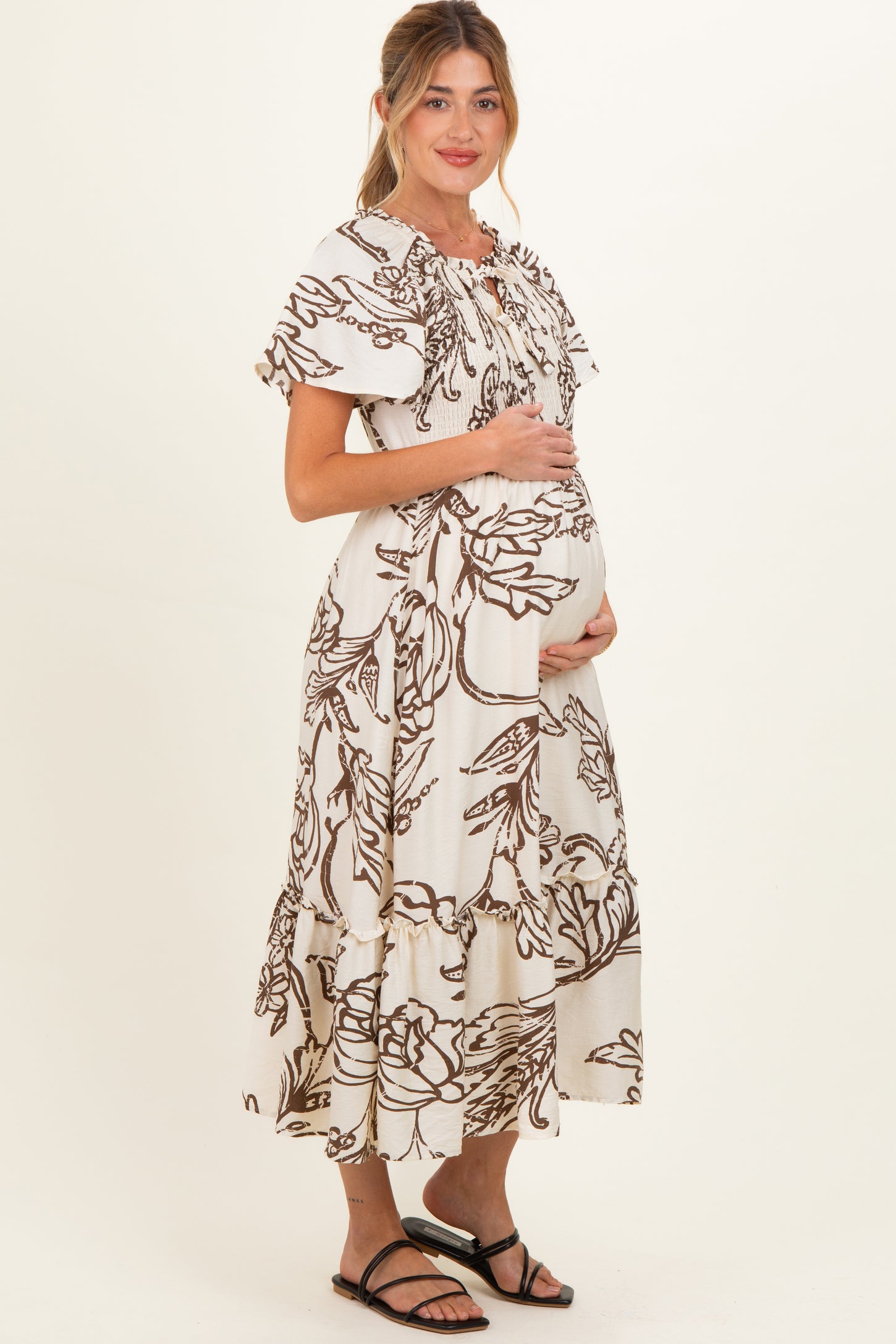 woman wearing a cream floral print maternity dress with flutter sleeves and a visible baby bump