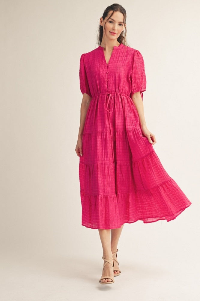 woman wearing a bright pink tiered maxi dress with short puff sleeves and a tie waist detail