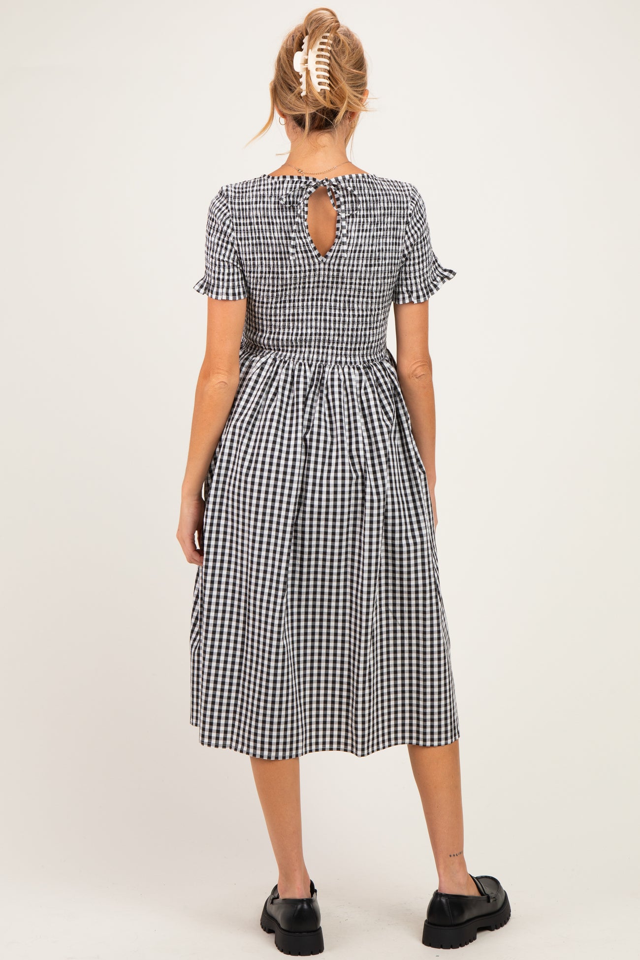 woman wearing a black and white gingham maternity dress with short ruffle sleeves and a keyhole back detail