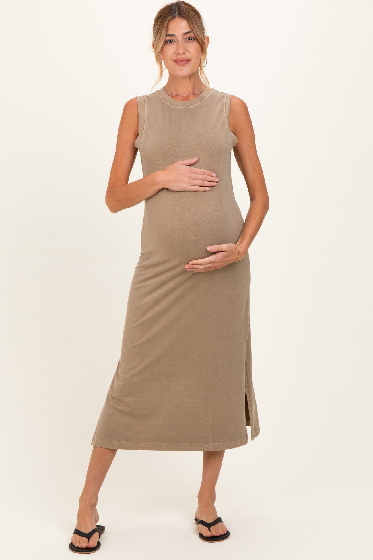 woman wearing a beige sleeveless maternity dress and holding her baby bump
