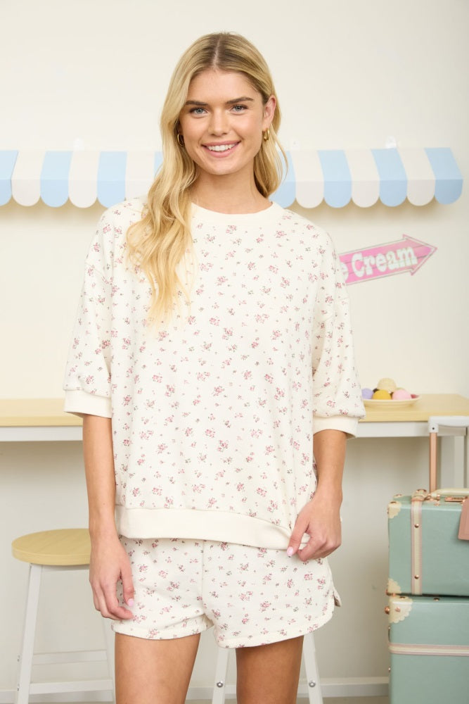 woman wearing a cream floral print sweatshirt and matching shorts in a casual setting