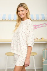 woman wearing a cream oversized sweatshirt with pink floral print and matching shorts, smiling and standing sideways