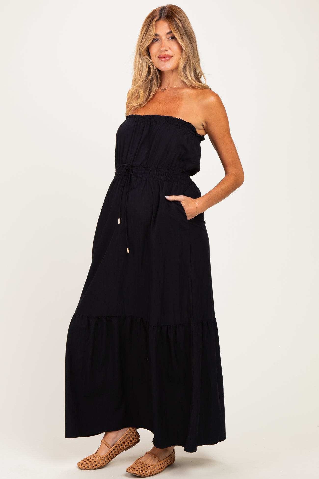 woman wearing a black strapless maternity maxi dress with a drawstring waist and pockets, standing confidently