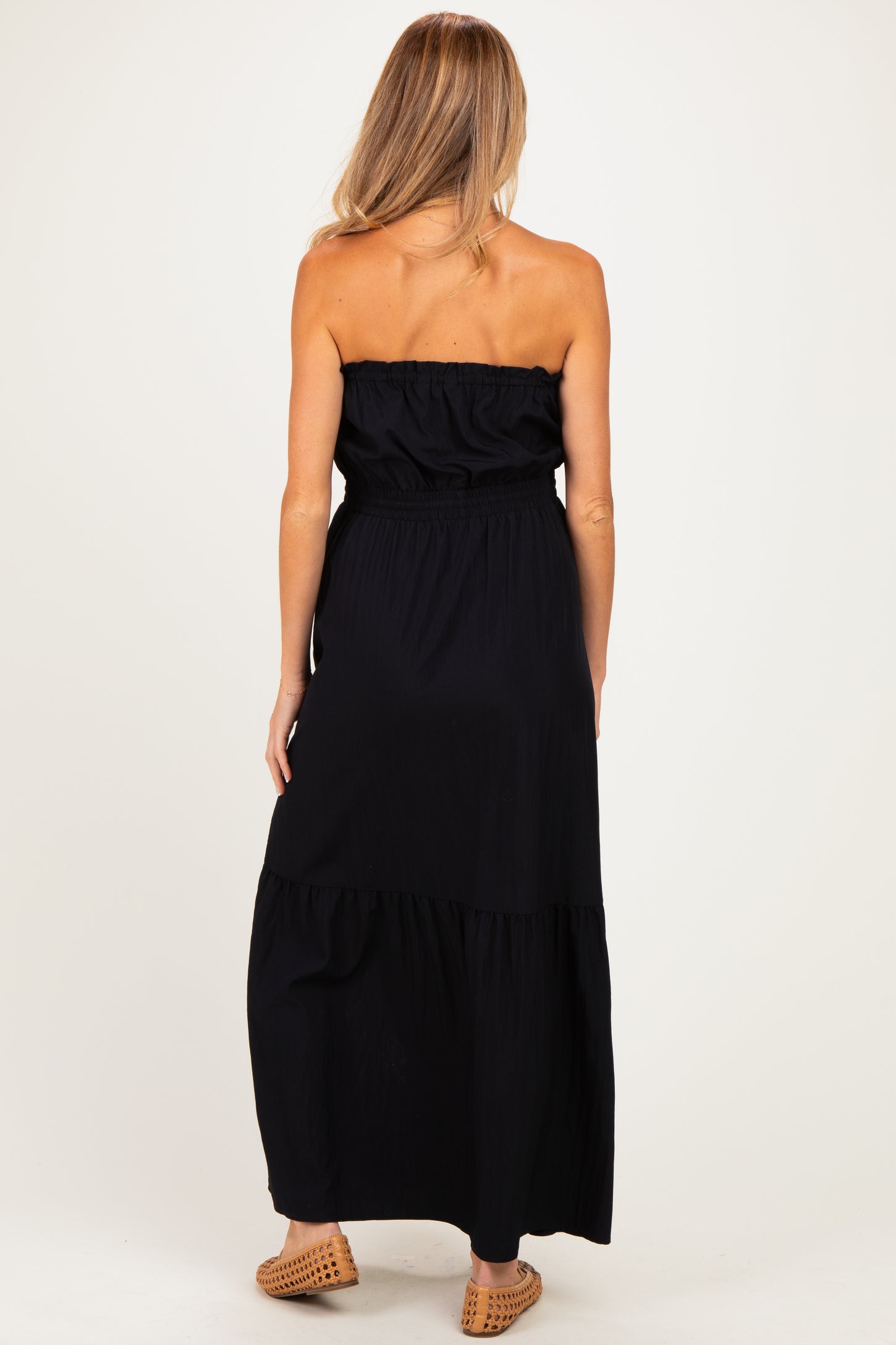 woman wearing a black strapless maternity maxi dress, showing a tiered design from the back