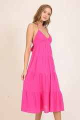 woman wearing a bright pink tiered midi dress with a halter neckline and back tie details