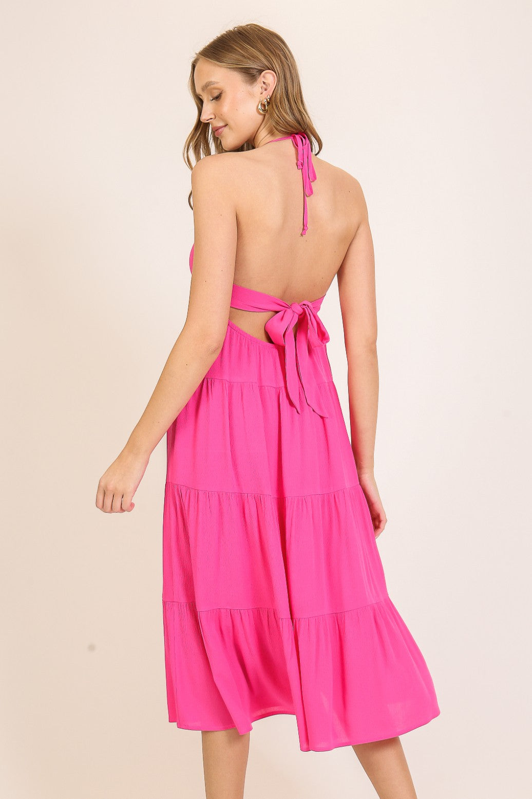 woman wearing a bright pink halter-neck tiered dress with an open back and tied detail