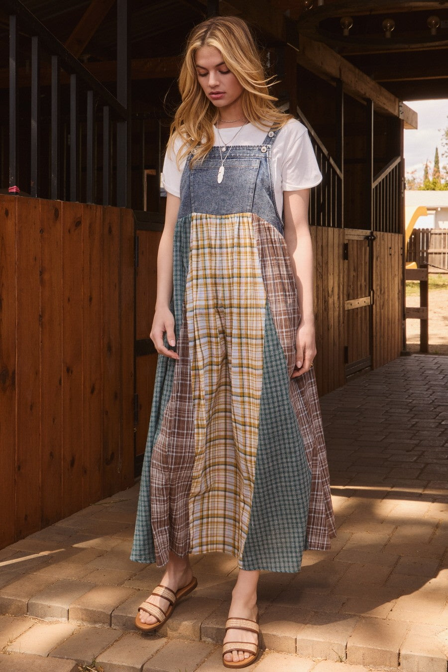 woman wearing a multi-patterned midi overall dress with a white t-shirt underneath and strappy sandals