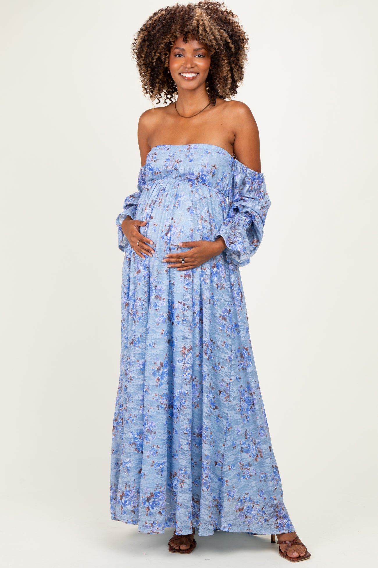 woman wearing a light blue off-the-shoulder floral maternity dress and cradling her baby bump