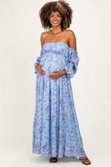 woman wearing a light blue off-the-shoulder floral maternity dress and cradling her baby bump