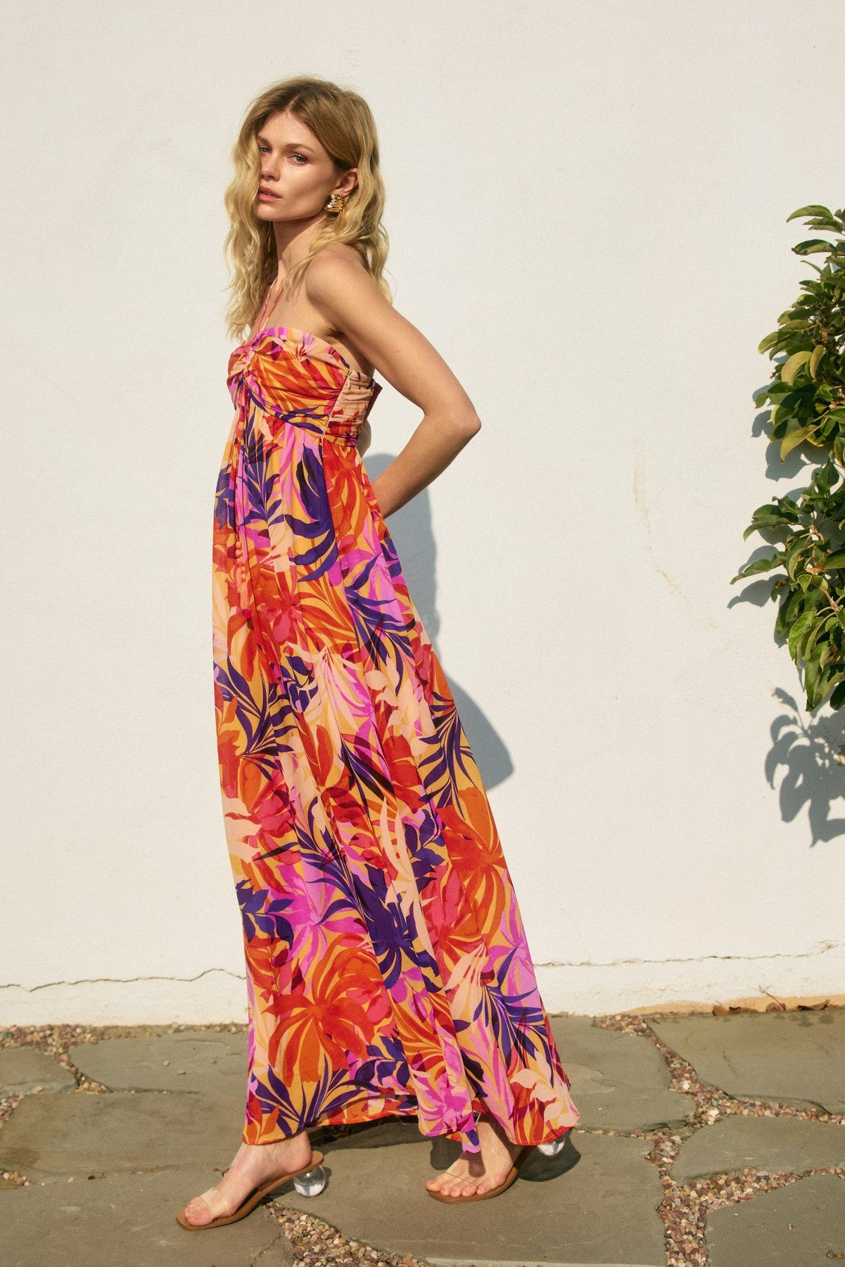 woman wearing a vibrant floral maxi dress in orange and pink tones, with a strapless design and a flowing silhouette