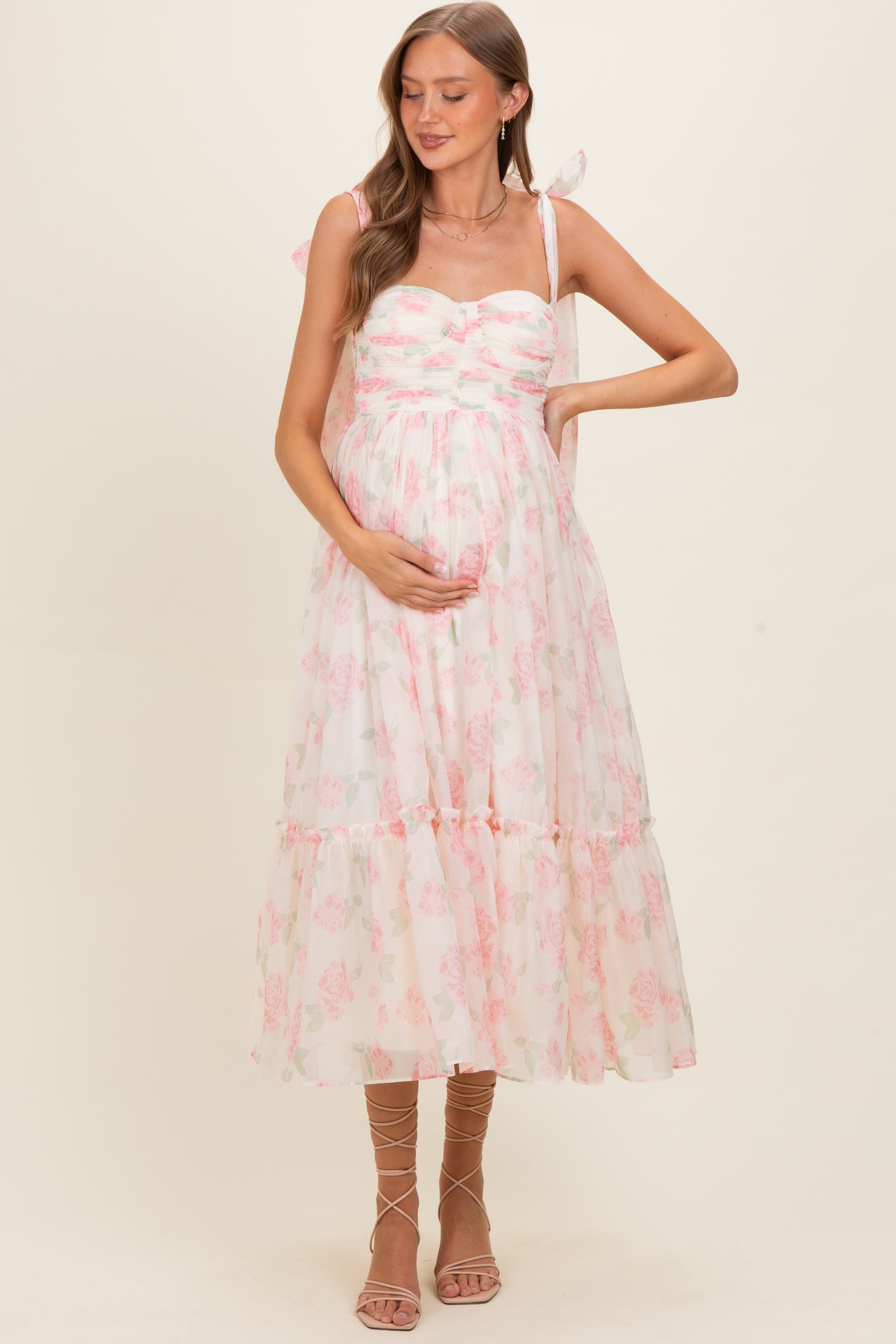 woman wearing a floral print maternity maxi dress with bow straps and holding her baby bump