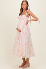 woman wearing a pink floral maternity dress with a flowy skirt and tie straps, showing her baby bump