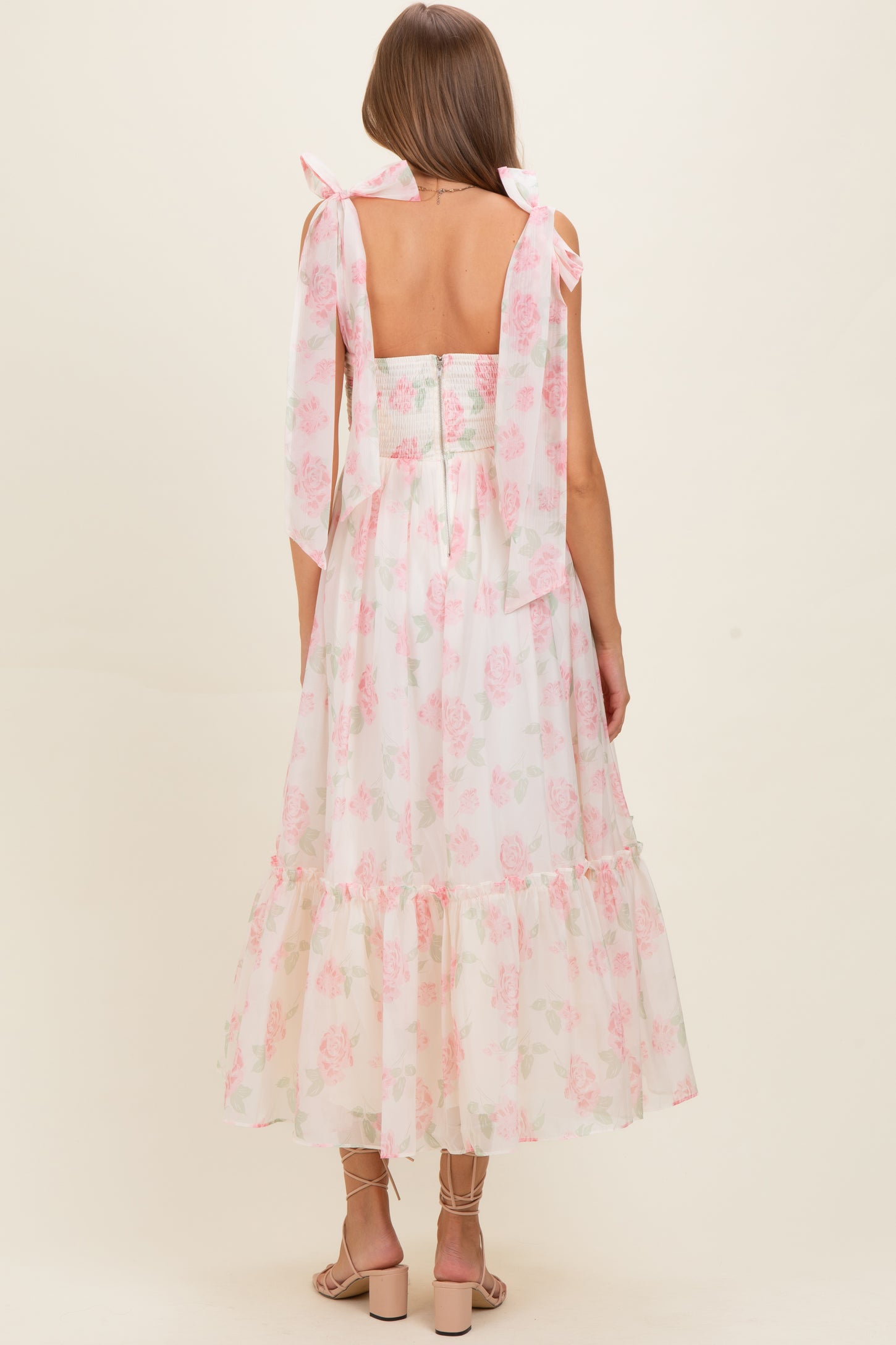 woman wearing a backless light pink floral maternity dress with flowy skirt and tied shoulder straps