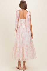 woman wearing a backless light pink floral maternity dress with flowy skirt and tied shoulder straps