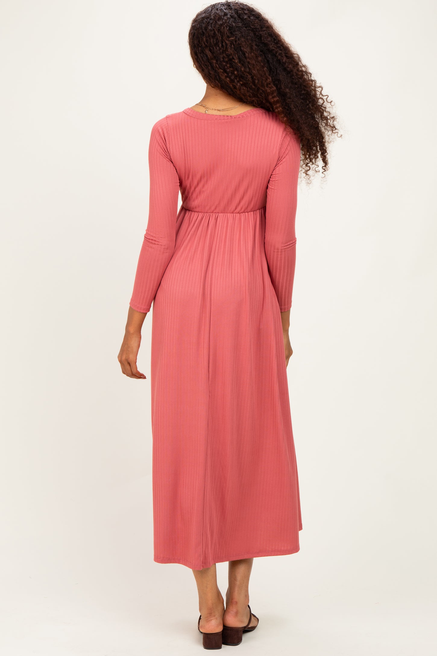 woman wearing a pink ribbed maxi dress with long sleeves and a fitted waist, viewed from the back