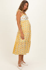 woman wearing a yellow and white striped maternity dress with floral print and adjustable tie straps, showing her baby bump