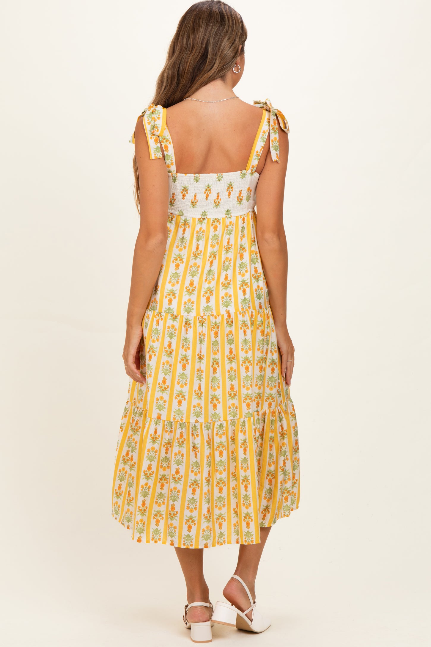 woman wearing a yellow floral patterned maternity dress with tie straps and a tiered skirt, showing her baby bump