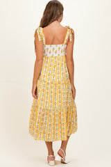 woman wearing a yellow floral patterned maternity dress with tie straps and a tiered skirt, showing her baby bump