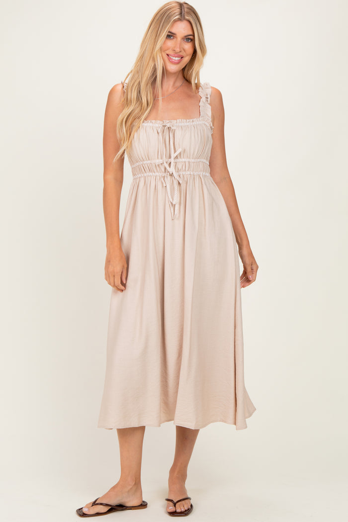 woman wearing a light beige maxi dress with adjustable straps and a drawstring waist, standing and smiling