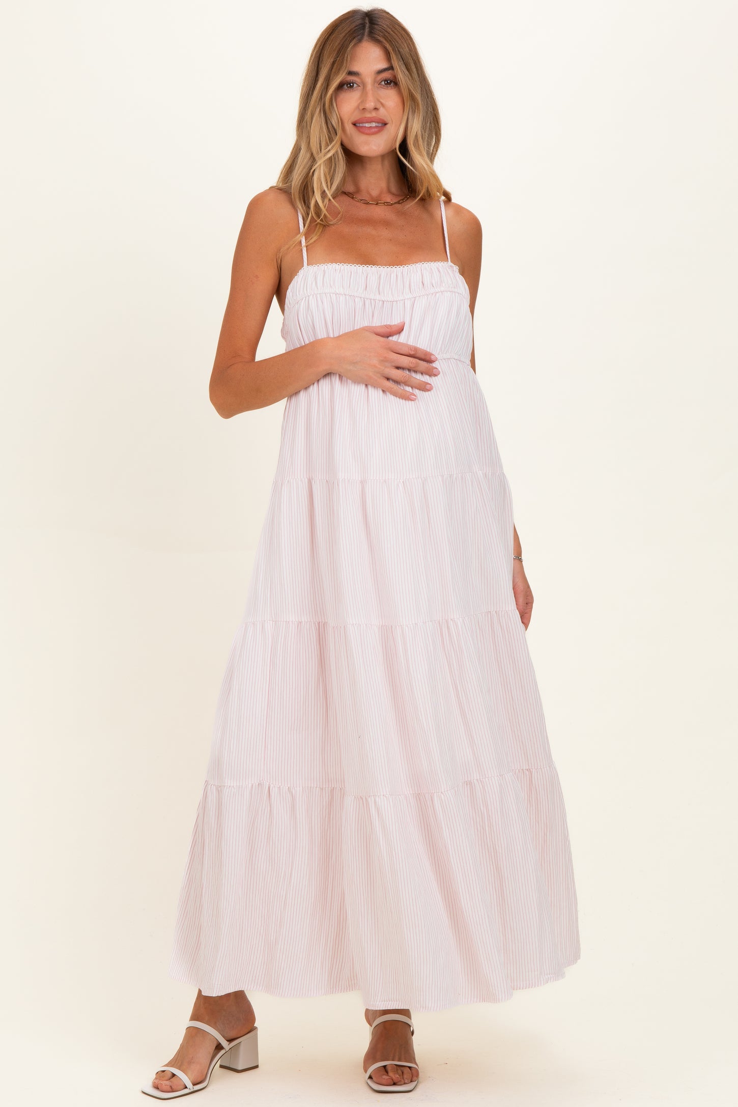 woman wearing a light pink striped maternity maxi dress and holding her baby bump