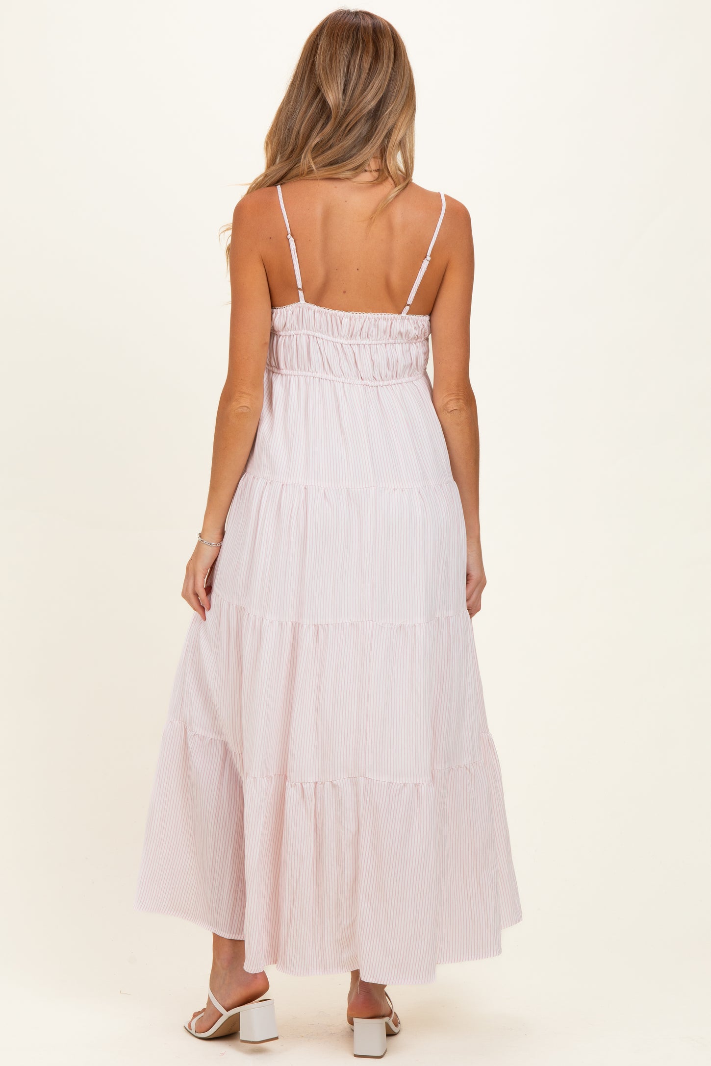 woman wearing a light pink striped maternity maxi dress with spaghetti straps and tiered skirt from the back