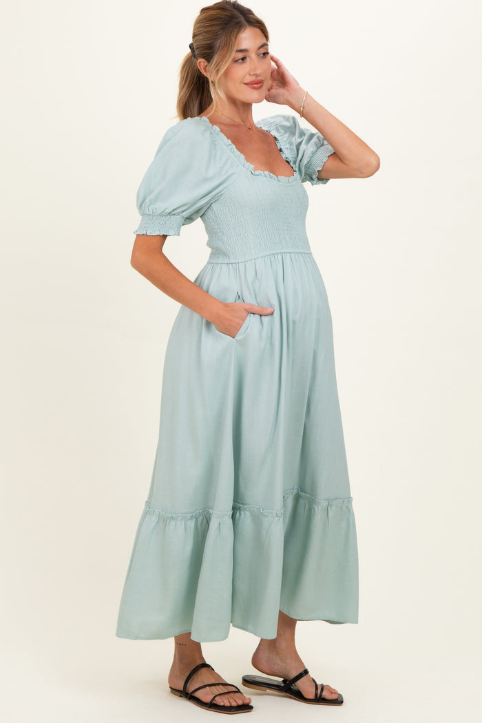 woman wearing a light green maternity dress with puff sleeves, a square neckline, and pockets, showcasing her baby bump