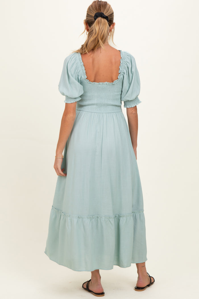 woman wearing a light green maternity dress with puff sleeves and a tiered skirt, showing a gathered back design