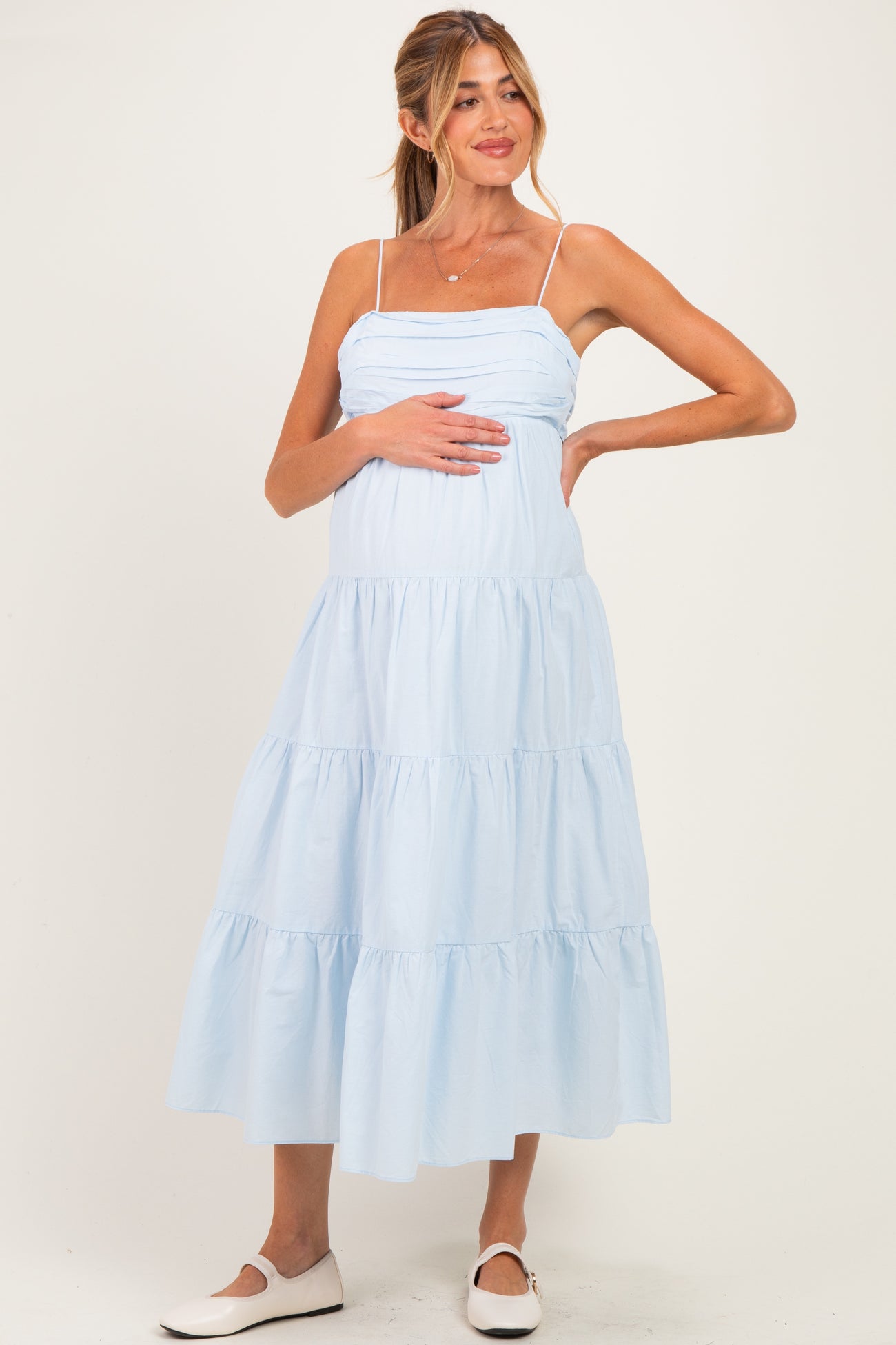 woman wearing a light blue maternity tiered midi dress and holding her baby bump