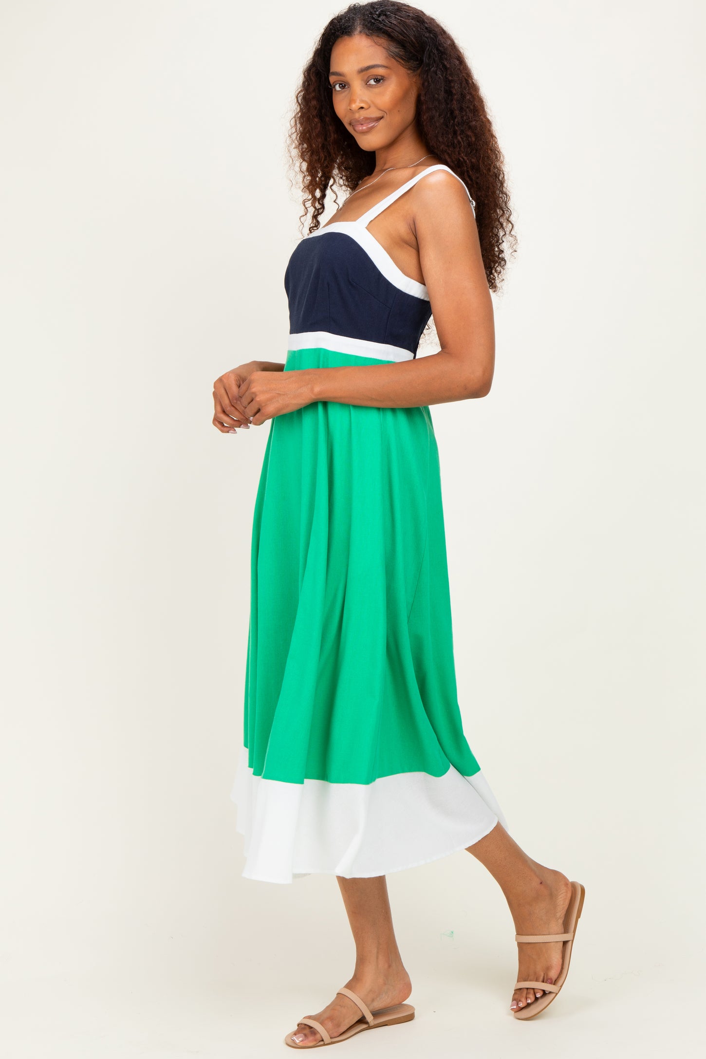 woman wearing a color-blocked maxi dress with a navy top, green midsection, and white bottom, styled with tan sandals