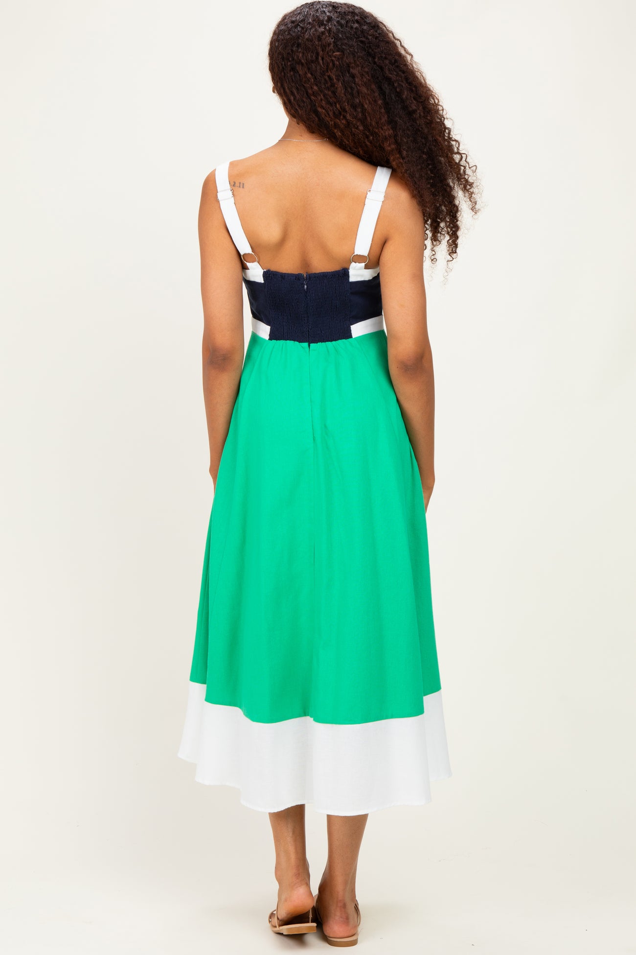 woman wearing a back view of a color-blocked green and navy midi dress with a fitted bodice and flowing skirt