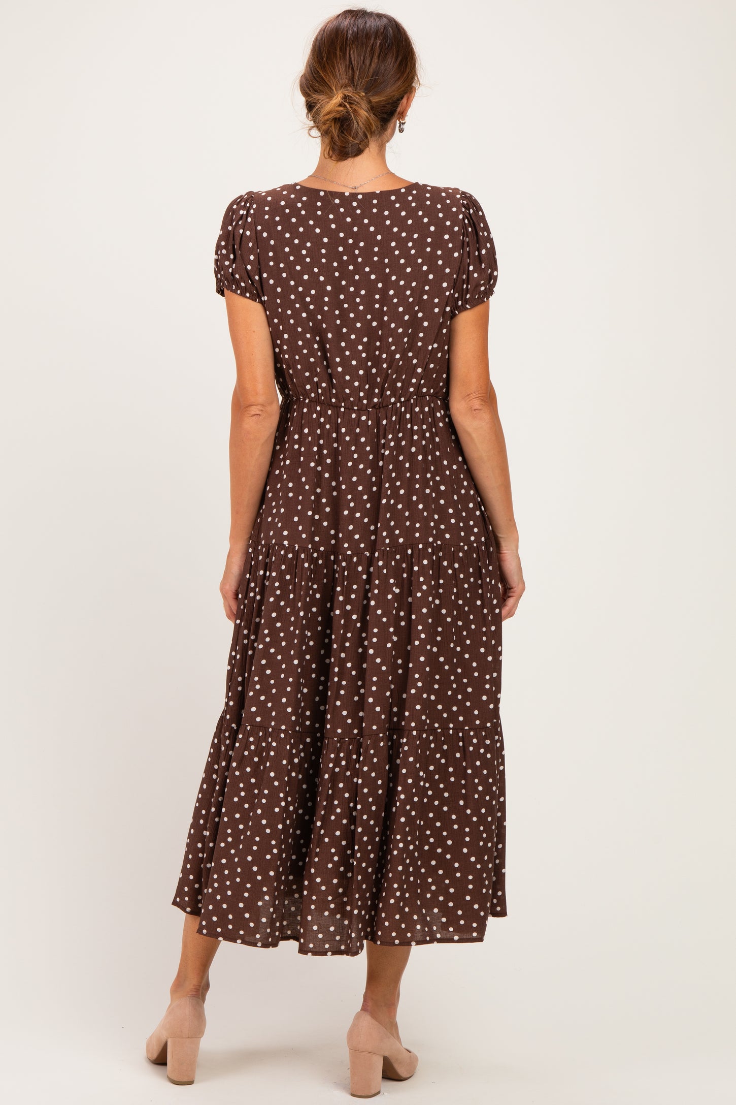 woman wearing a brown polka dot maxi dress with short sleeves and a tiered skirt, facing away from the camera