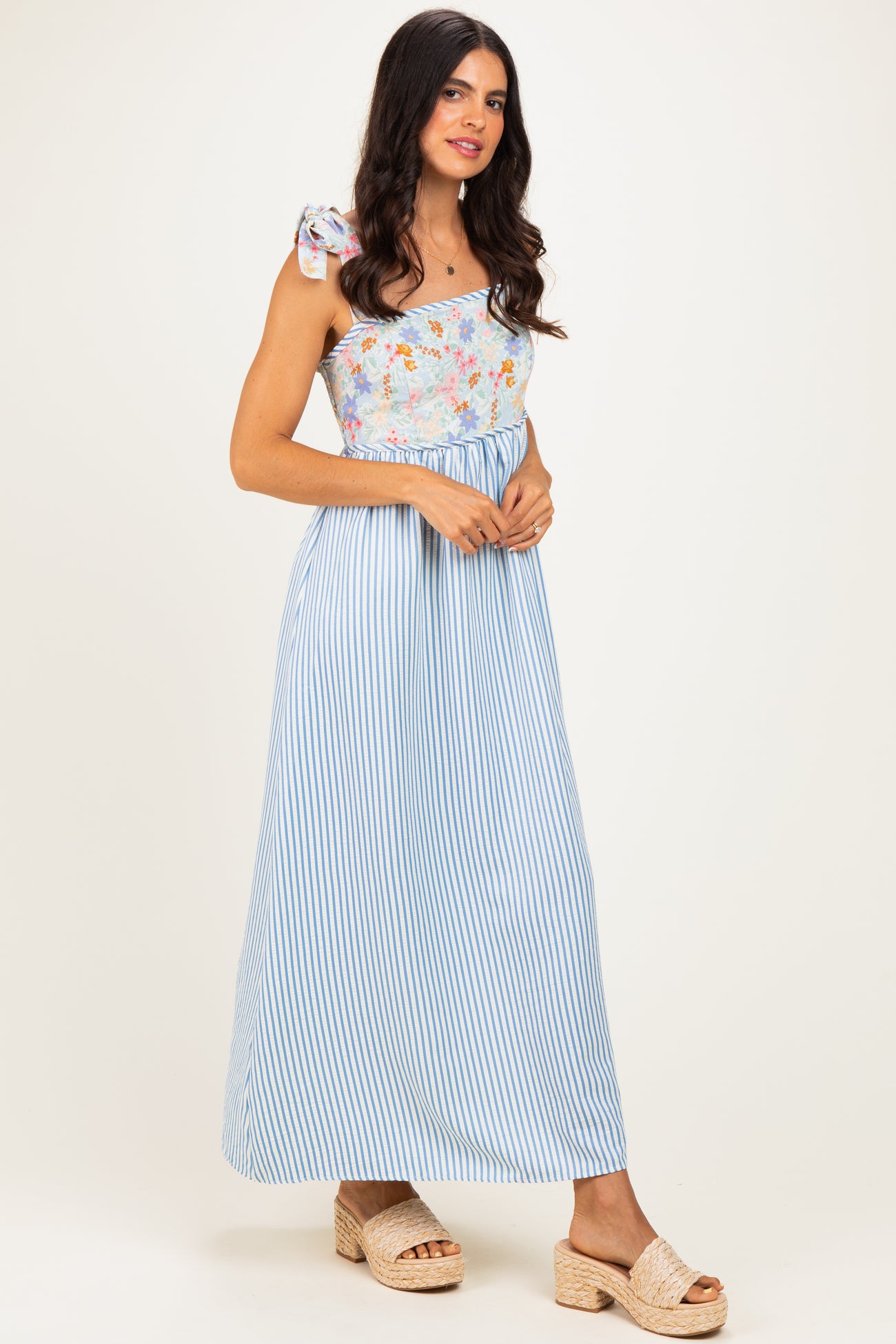 woman wearing a blue and white striped maxi dress with a floral one-shoulder top and a bow detail on the strap