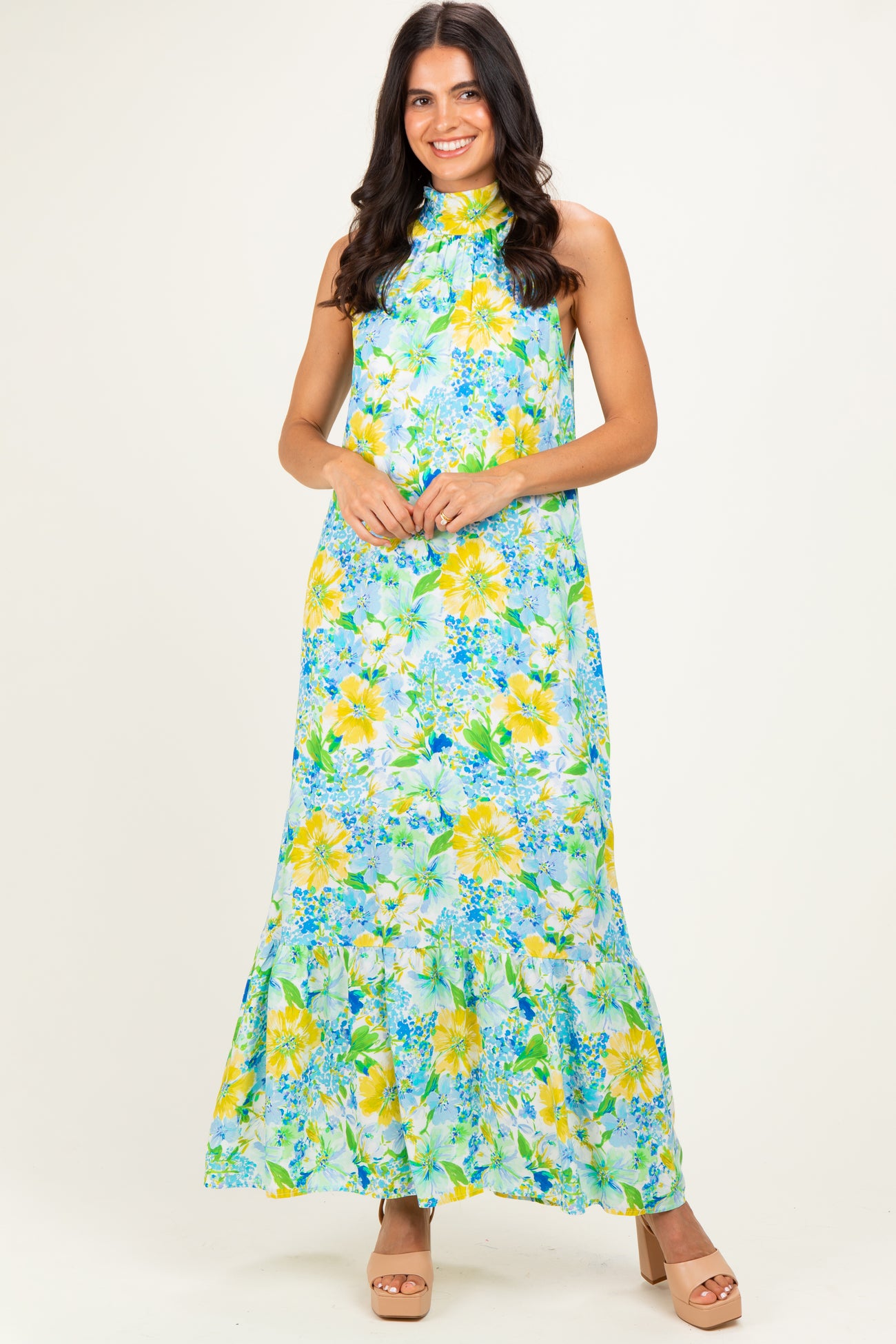 woman wearing a floral maxi dress in greens and yellows with a halter neck and tiered hem