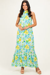 woman wearing a floral maxi dress in greens and yellows with a halter neck and tiered hem