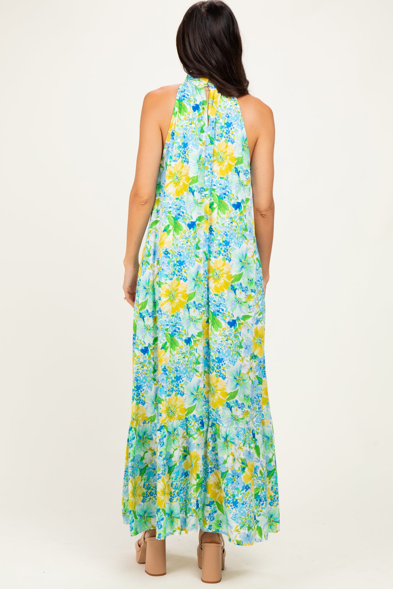 woman wearing a floral maxi dress with a halter neck in shades of blue and yellow, seen from the back