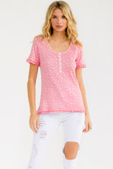woman wearing a pink short sleeve top with a heart pattern and button details, paired with white ripped jeans