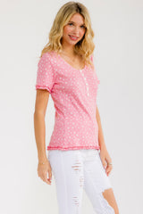 woman wearing a pink short sleeve top with a floral pattern and ruffle details, paired with distressed white jeans
