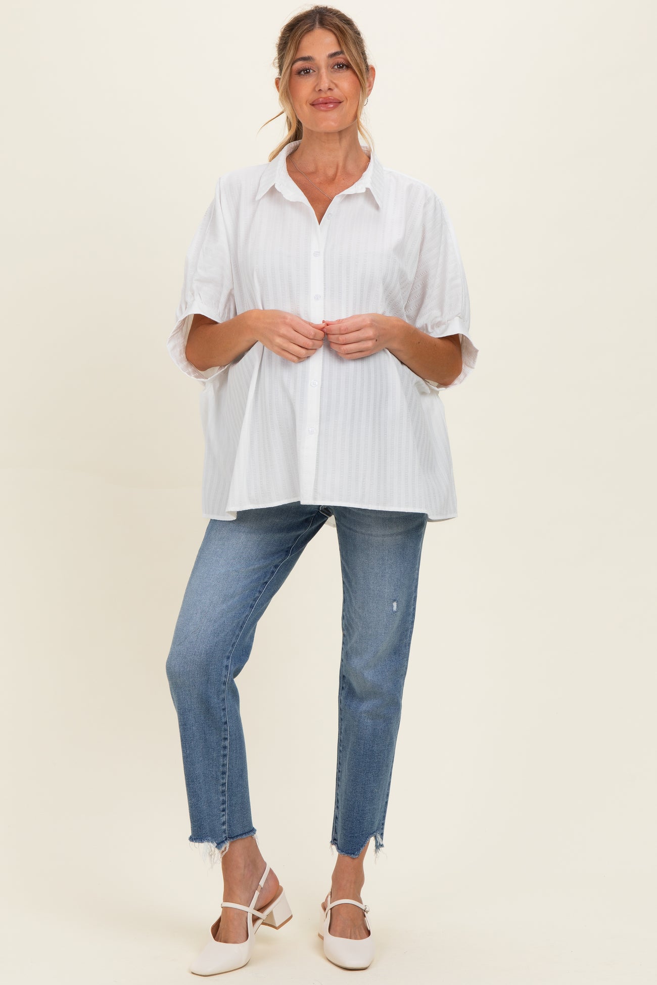 woman wearing a white striped maternity button-up shirt with loose sleeves and distressed blue maternity jeans
