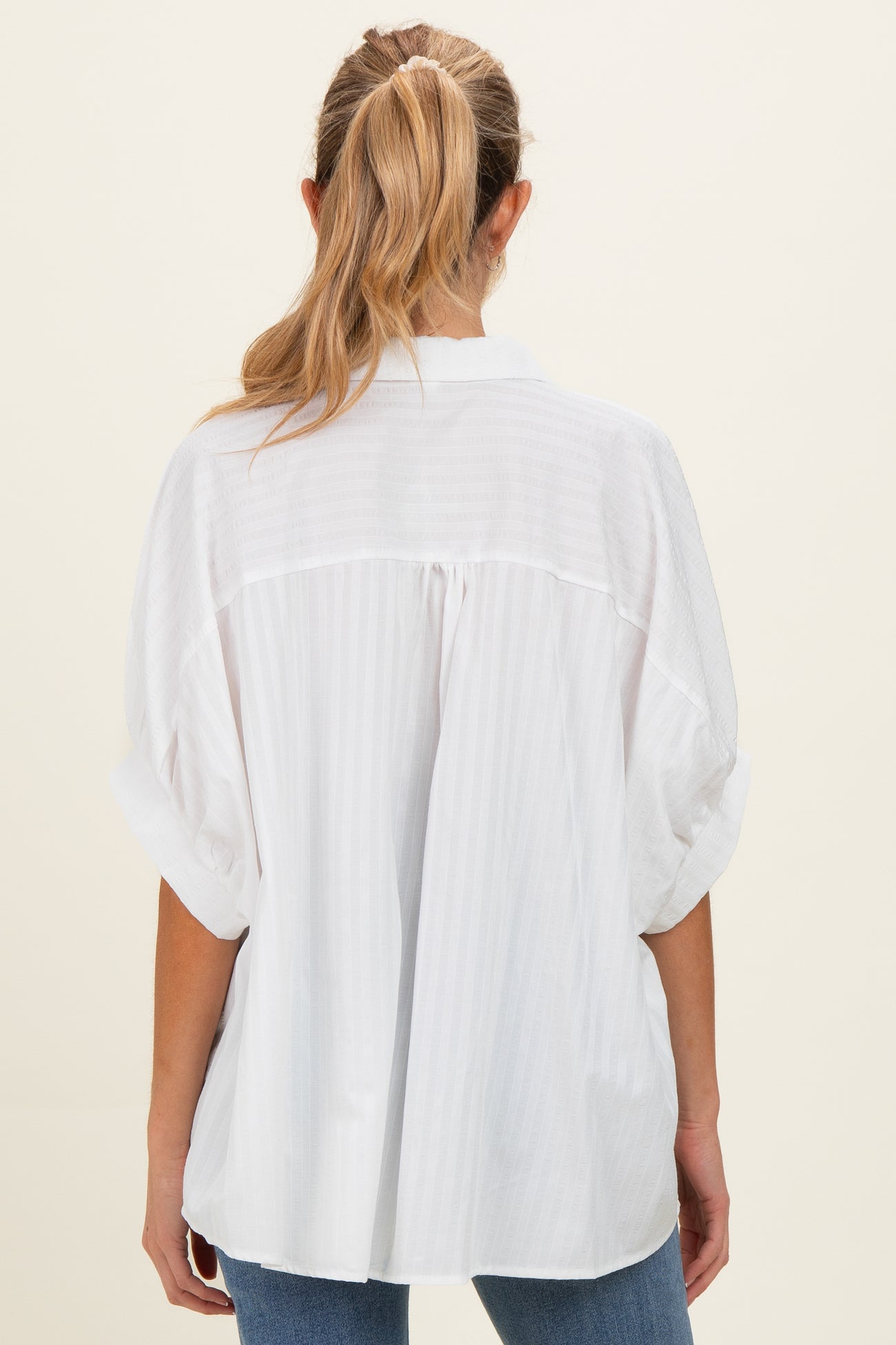 woman wearing a white striped oversized maternity top, viewed from the back, with rolled short sleeves